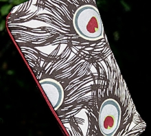 photo of closed zip pouch made by Homegrown Crafts out of a repurposed dinner napkin with dark grey and silver peacock feather print and red zipper