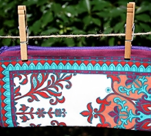 photo of closed zip pouch made by Homegrown Crafts out of a repurposed dinner napkin with multi color print with blue lining and maroon zipper