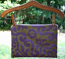 photo of closed zip pouch made by Homegrown Crafts out of a repurposed placemat with army green material and purple print with light purple zipper