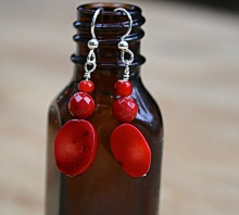 Red coral drop earrings displayed on a bottle
